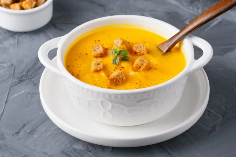 Cream of pumpkin soup with croutons in a white porcelain crock.
