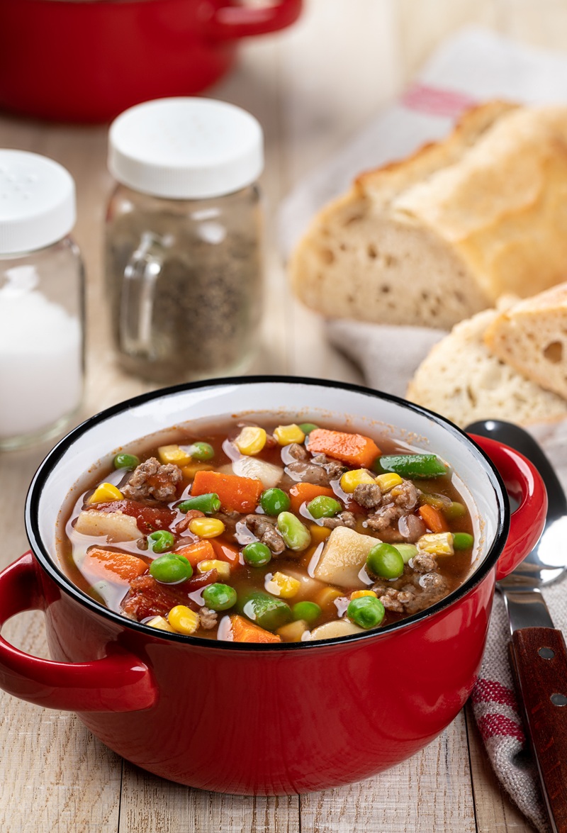 Vegetable beef soup in a red bowl on a rustic wooden table