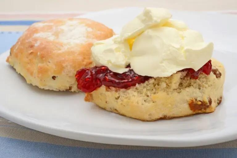 Homemade clotted cream recipe pictured on top of strawberry jam and a scone.