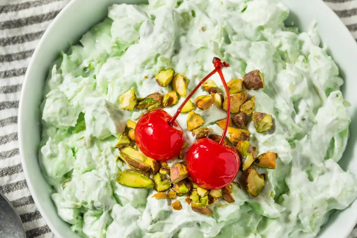 Green Watergate salad topped with chopped nuts and maraschino cherries