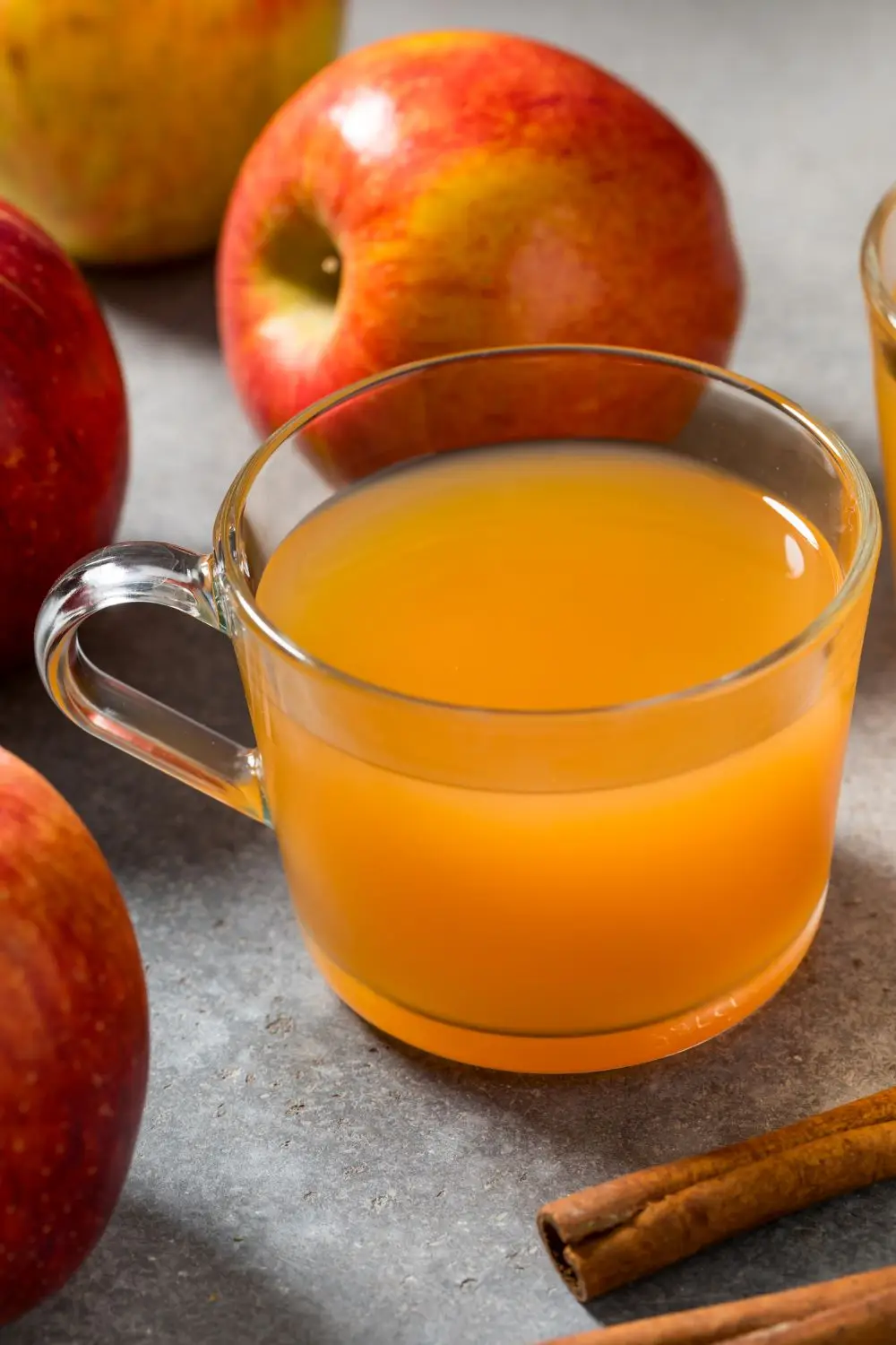 Hot mulled apple cider in a clear mug surrounded by red apples