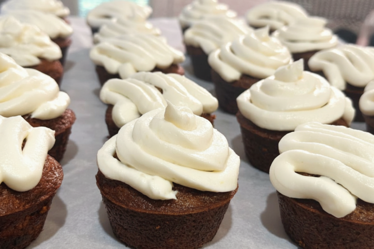 Rows of spiced carrot cupcakes topped with cream cheese frosting.