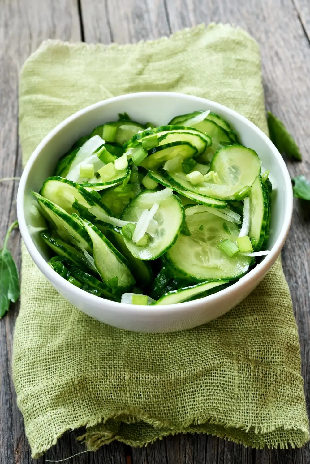 viennese cucumber salad in a white bowl sitting on a sage green burlap napkin