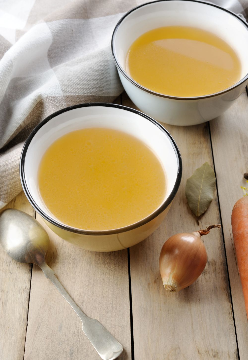 Homemade broth in the bowls on the rustic background.