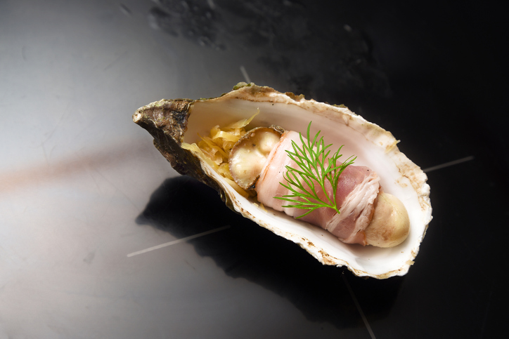 fresh baked oyster wrapped with bacon and dill garnish in the shell; appetizer called angel on horseback