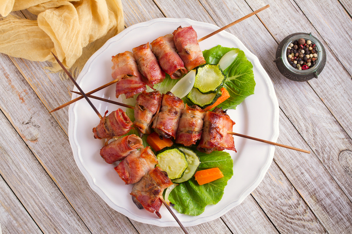 Chicken liver wrapped with bacon on skewers. Grilled liver kebabs with vegetables. View from above, top studio shot