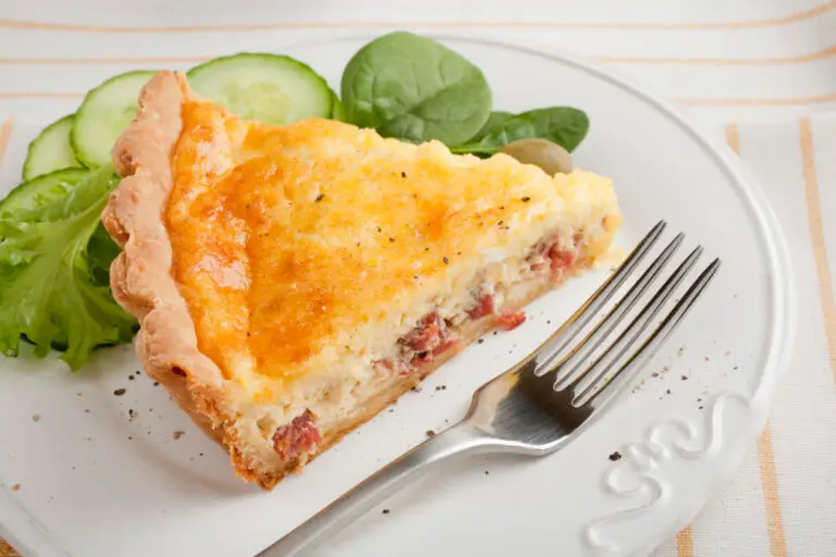 slice of classic quiche lorraine on a white plate served with a green salad