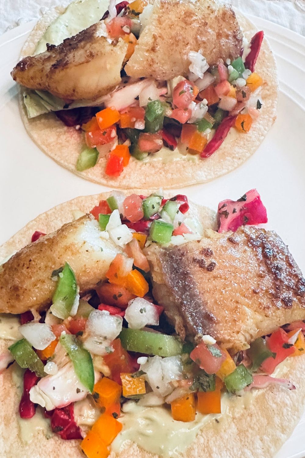 two baja fish tacos with pan seared cod, cabbage slaw, pico de gallo, and creamy avocado sauce