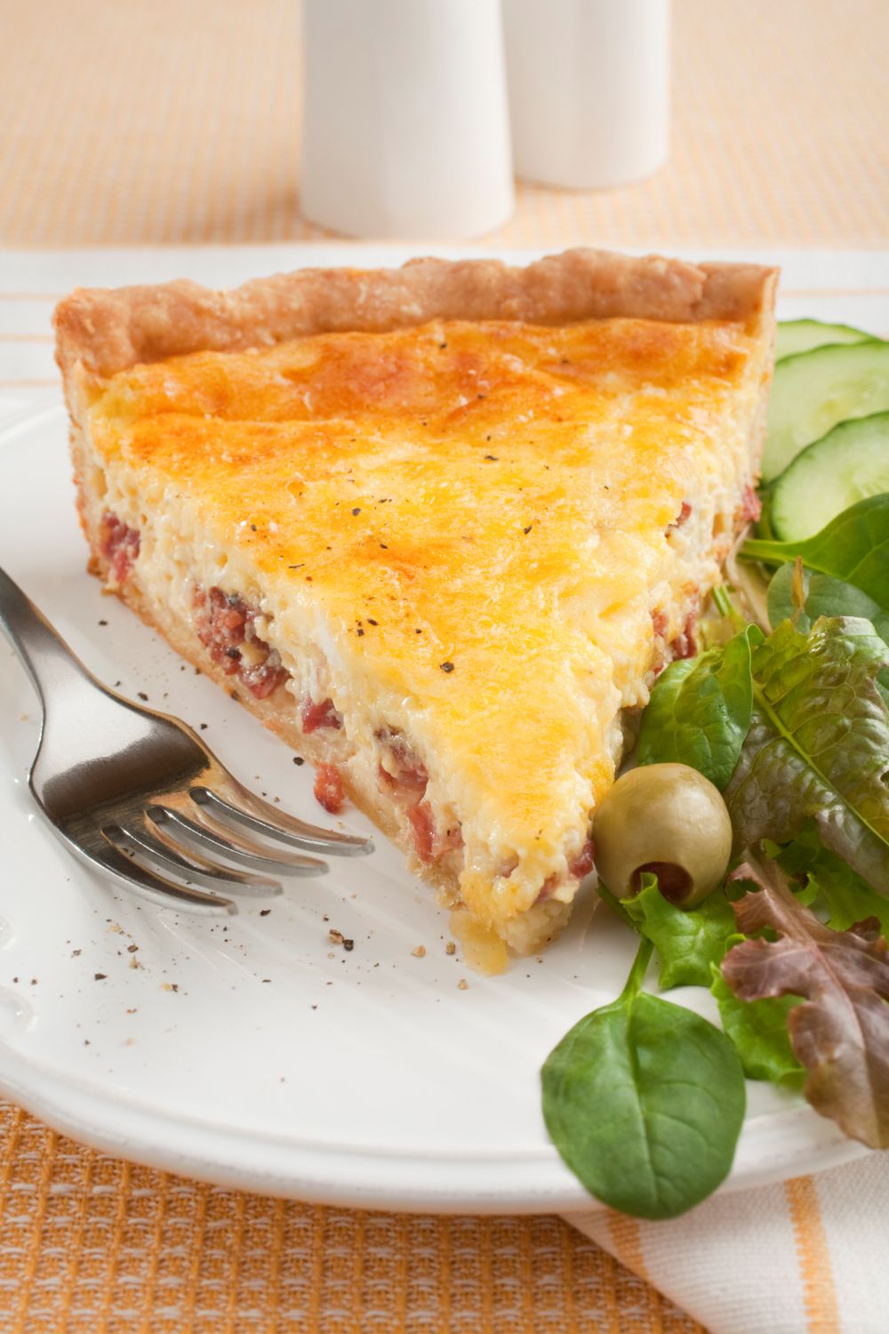 slice of classic quiche lorraine on a white plate served with a green salad