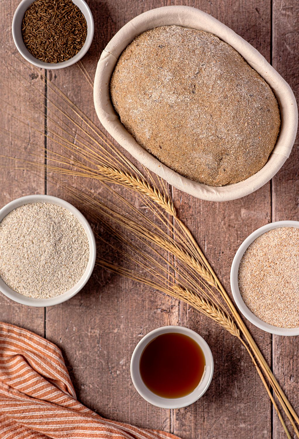 german farmers bread rising in a proofing basket surrounded by ingredients