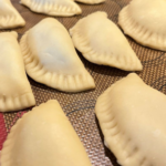 tray of uncooked, crimped pierogies ready to boil
