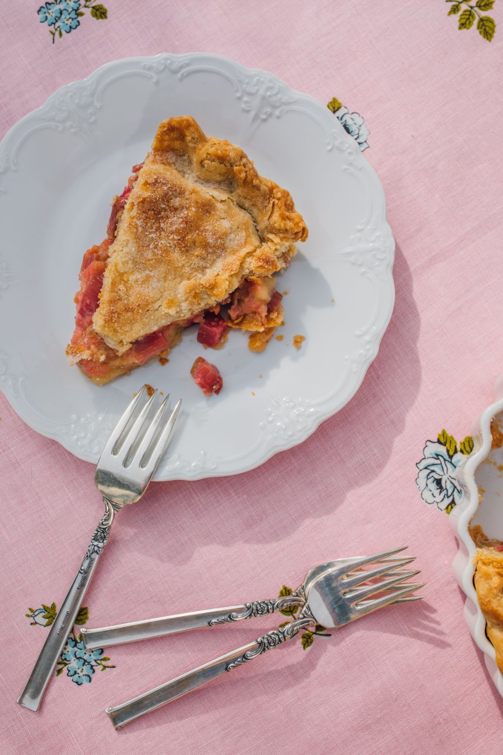 old fashioned rhubarb pie with one slice missing on a vintage pink tablecloth