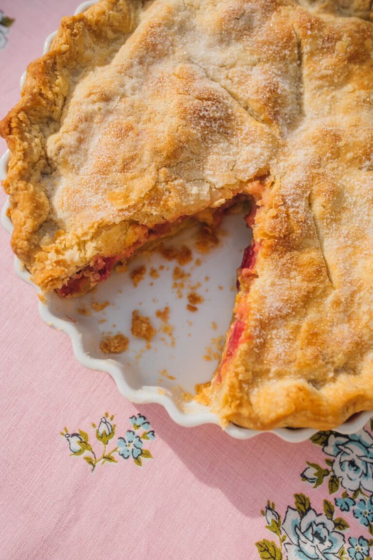 old fashioned rhubarb pie with one slice missing on a vintage pink tablecloth