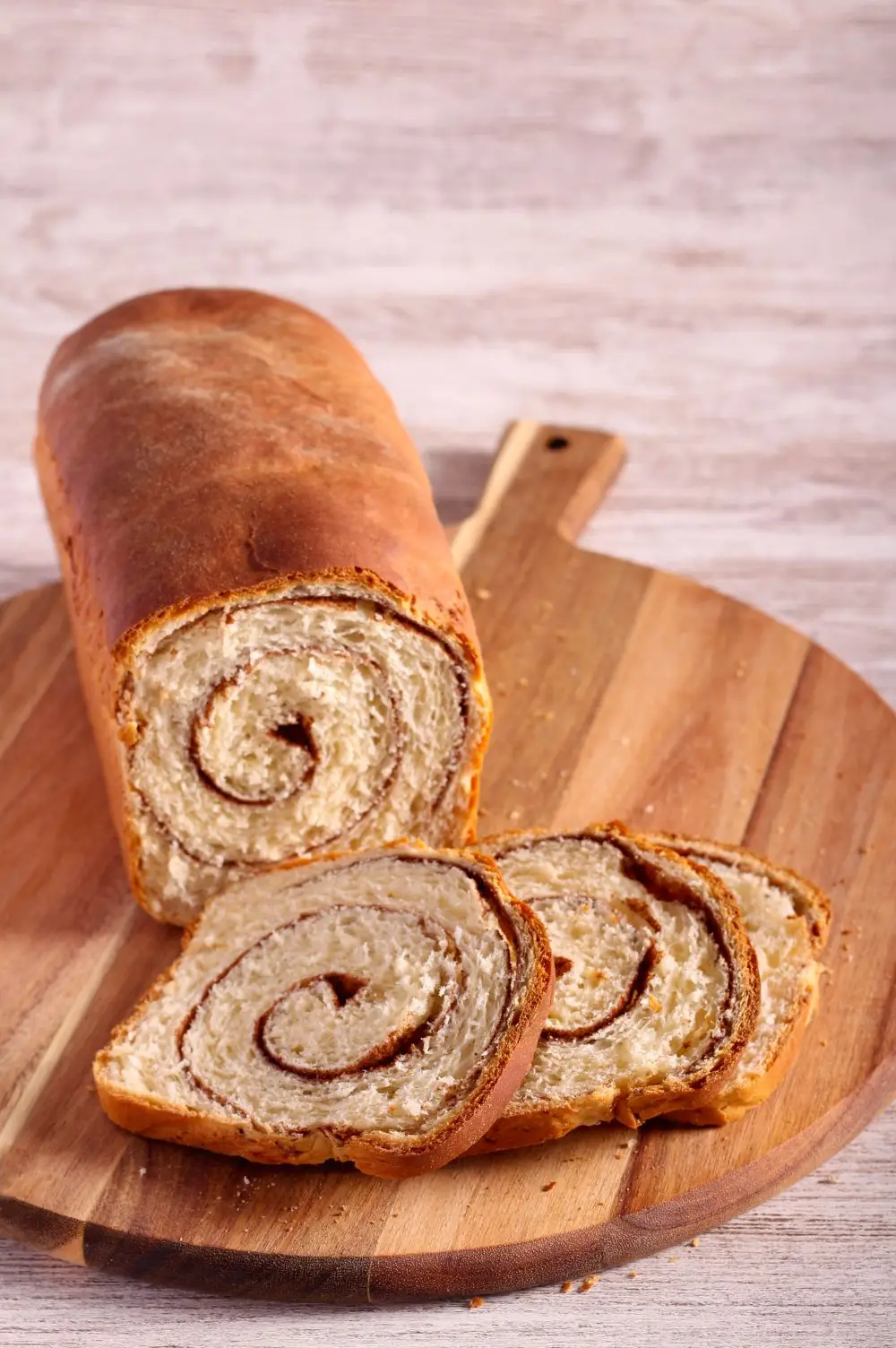 sliced loaf of cinnamon swirl bread on a round wooden cutting board